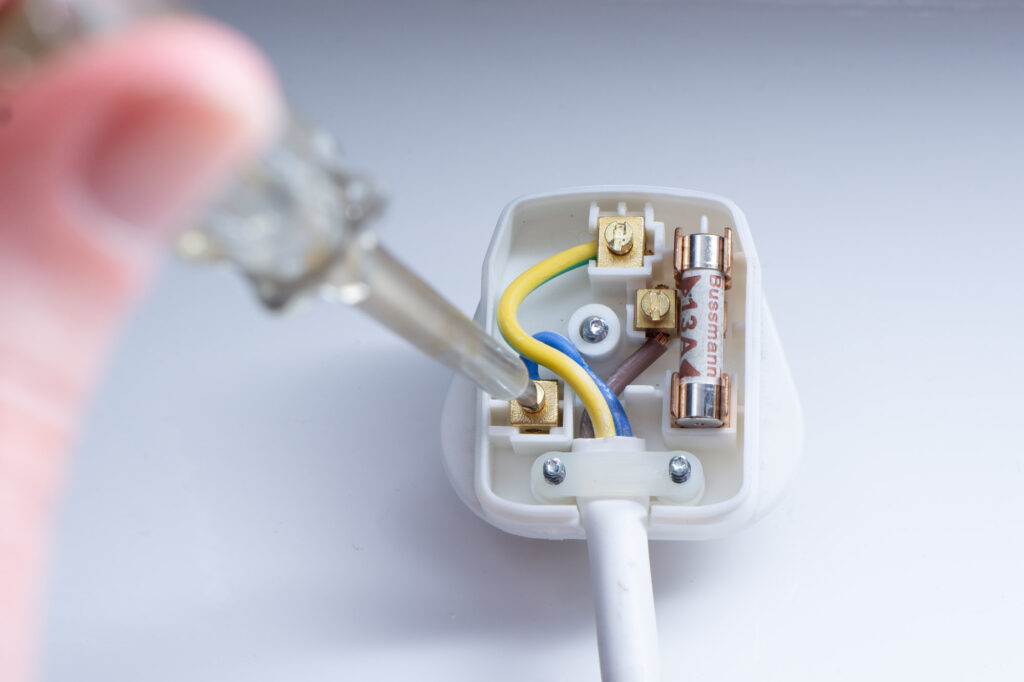Rewirable 13A British plug with the cover removed. An electrical screwdriver is being used to check the terminals are secure.