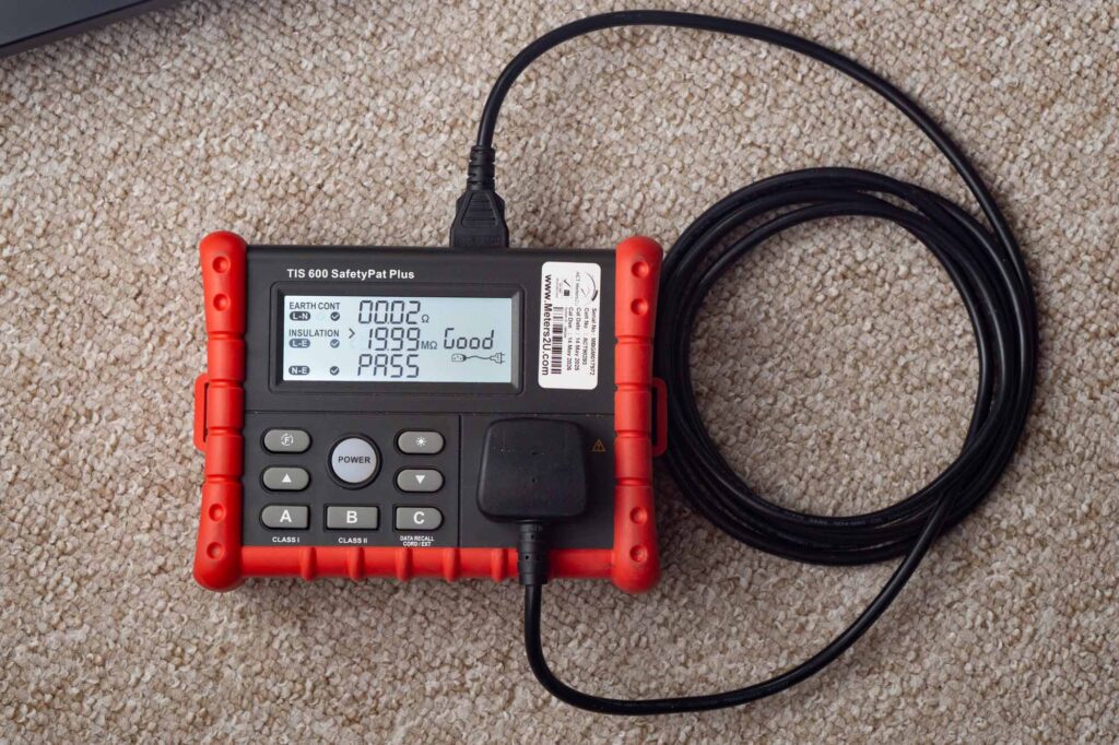 PAT test machine with an IEC mains cable attached having completed successful testing. The electrical readings and test results are shown on the display.