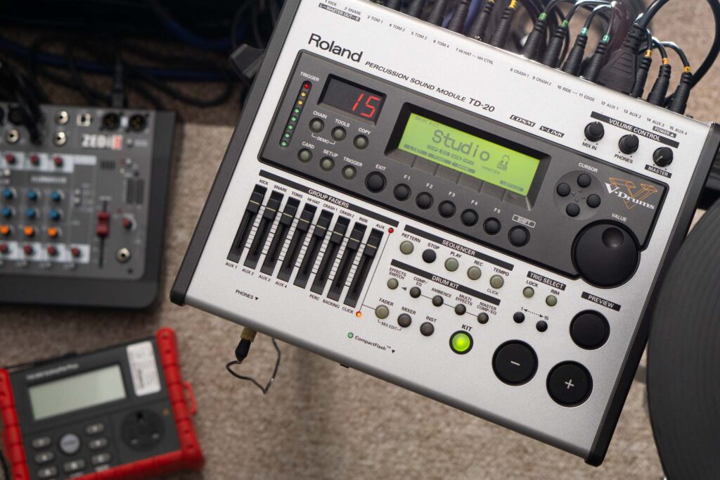 Image shows a powered on Roland TD-20 drum module with a PAT test machine out of focus in the background on the floor. This is the function test (checking the device powers on and works).